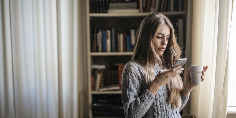 Kvinde med kaffe, der ser på mobil for at finde oversigt over danske forsikringsselskaber